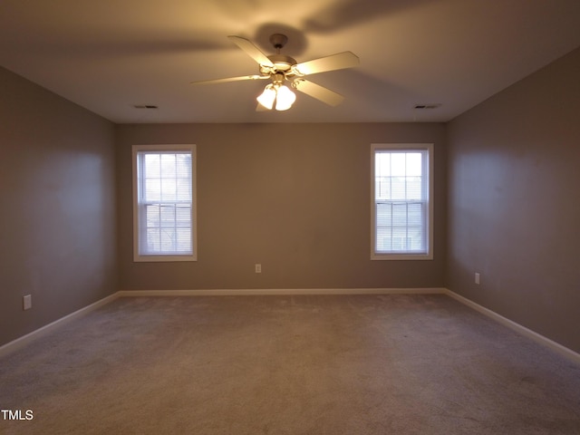 carpeted spare room with visible vents, a ceiling fan, and baseboards