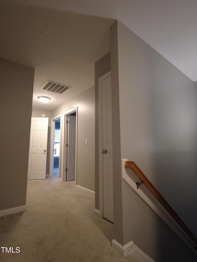 hallway with visible vents, an upstairs landing, baseboards, and light carpet