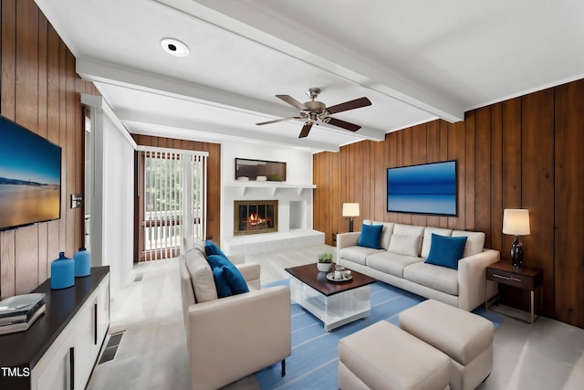 living area with a glass covered fireplace, beamed ceiling, wood walls, and a ceiling fan