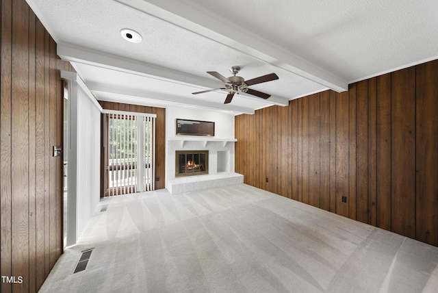 unfurnished living room featuring beam ceiling, visible vents, wood walls, and a textured ceiling