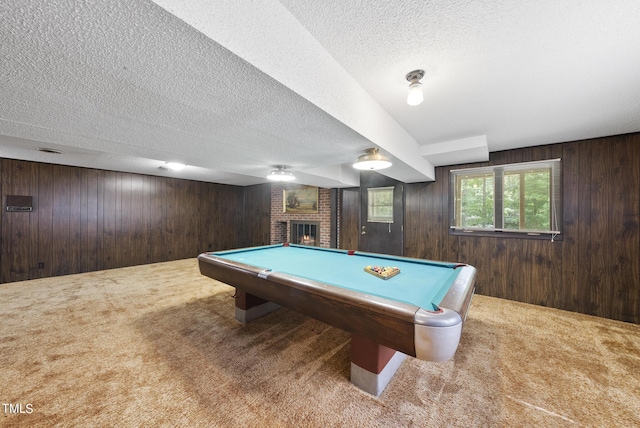 recreation room with wooden walls, carpet, pool table, a textured ceiling, and a brick fireplace