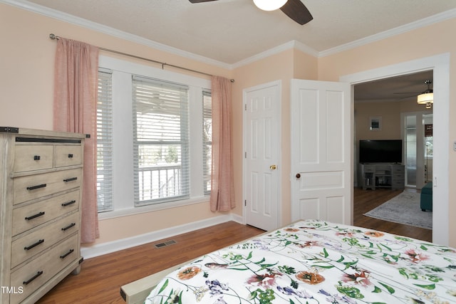 bedroom featuring visible vents, crown molding, baseboards, wood finished floors, and a ceiling fan