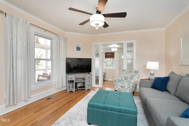 living room with ornamental molding, wood finished floors, visible vents, and a healthy amount of sunlight