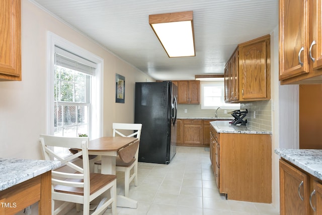 kitchen featuring brown cabinetry, a sink, decorative backsplash, and black refrigerator with ice dispenser