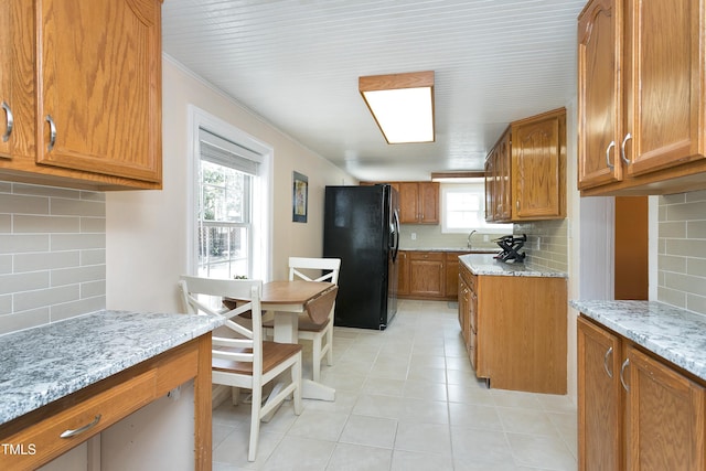 kitchen featuring light stone countertops, light tile patterned floors, freestanding refrigerator, brown cabinetry, and a sink