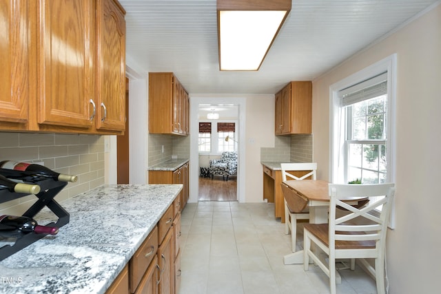 kitchen with light tile patterned floors, backsplash, brown cabinetry, and light stone countertops