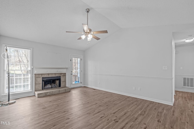 unfurnished living room with a tiled fireplace, visible vents, vaulted ceiling, and wood finished floors