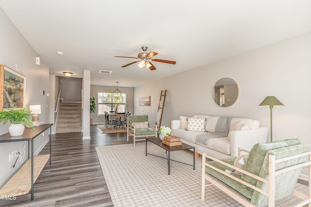 living area with ceiling fan, wood finished floors, visible vents, baseboards, and stairway