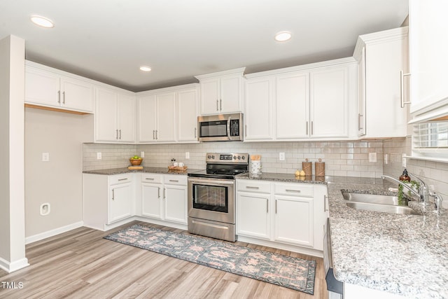 kitchen with stainless steel appliances, a sink, white cabinetry, light wood-type flooring, and tasteful backsplash