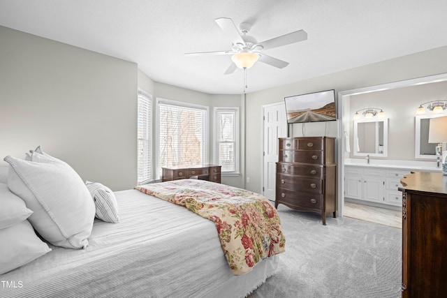 bedroom with light colored carpet, ceiling fan, a sink, ensuite bath, and a textured ceiling