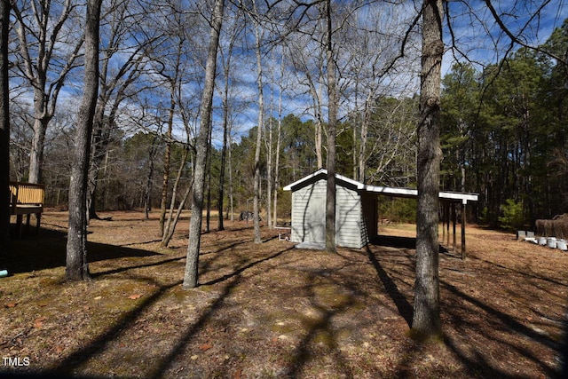 view of yard featuring a deck, an outbuilding, a view of trees, and a shed