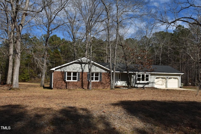 single story home featuring a garage, dirt driveway, a view of trees, and brick siding