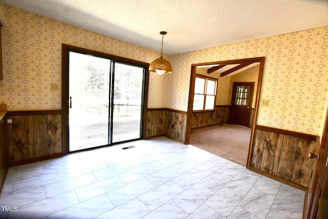 unfurnished room with wallpapered walls, visible vents, wainscoting, marble finish floor, and a textured ceiling