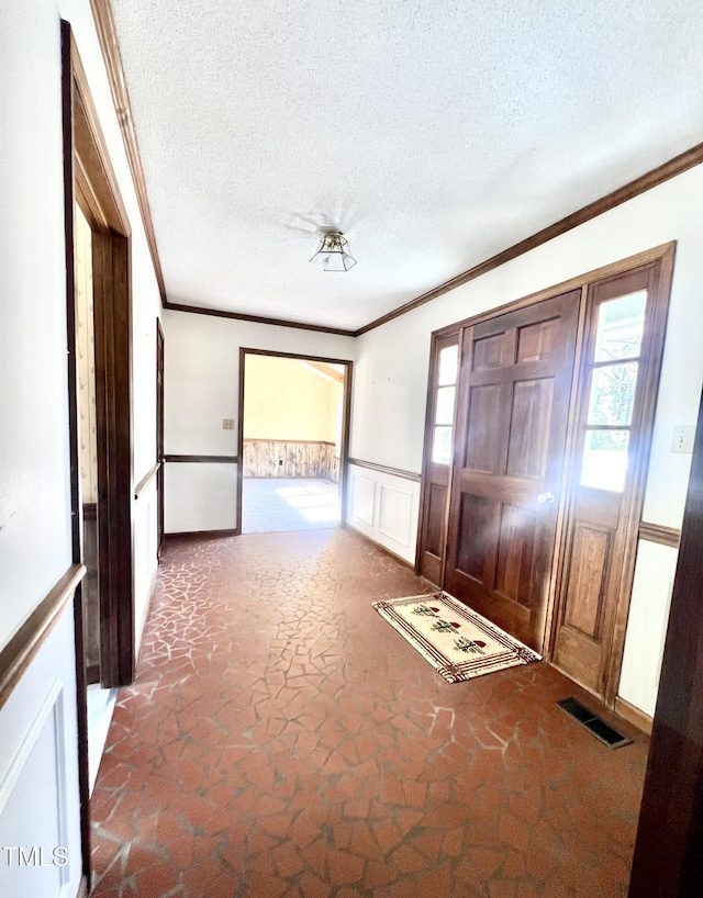 entrance foyer featuring a textured ceiling, ornamental molding, wainscoting, and visible vents