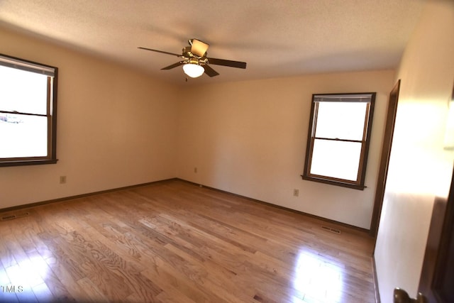 empty room with a ceiling fan, visible vents, light wood-style flooring, and baseboards