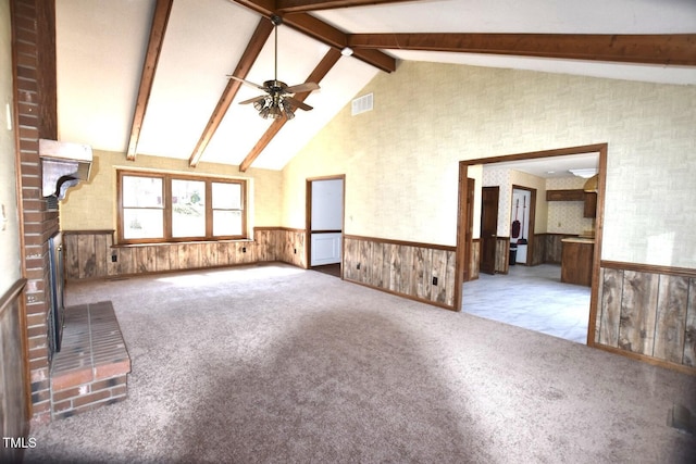 unfurnished living room featuring carpet, a wainscoted wall, beamed ceiling, and visible vents