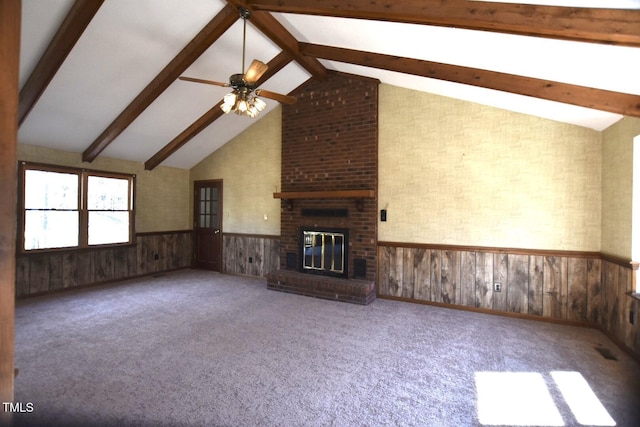 unfurnished living room featuring a wainscoted wall, a ceiling fan, a brick fireplace, beamed ceiling, and carpet