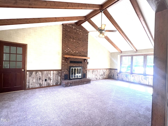 unfurnished living room featuring carpet floors, a wainscoted wall, vaulted ceiling with beams, a fireplace, and ceiling fan