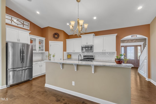 kitchen featuring arched walkways, stainless steel appliances, white cabinetry, vaulted ceiling, and dark wood finished floors