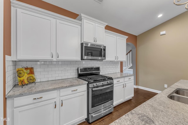 kitchen featuring decorative backsplash, appliances with stainless steel finishes, dark wood-type flooring, white cabinetry, and baseboards