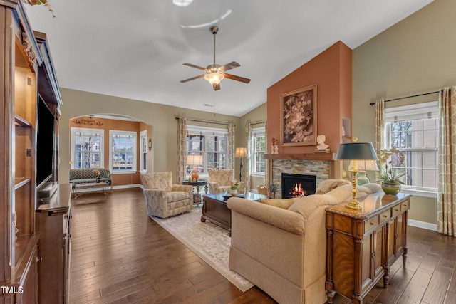 living room featuring arched walkways, dark wood-style flooring, a fireplace, and plenty of natural light