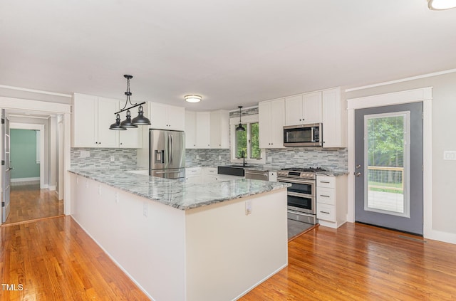 kitchen with a peninsula, white cabinetry, hanging light fixtures, appliances with stainless steel finishes, and light wood finished floors