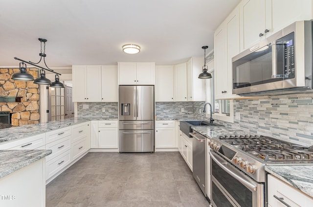 kitchen with decorative light fixtures, appliances with stainless steel finishes, white cabinets, a sink, and light stone countertops