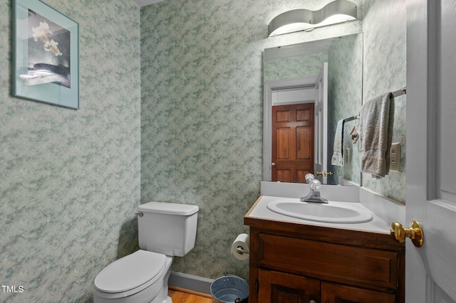 half bathroom with toilet, wallpapered walls, baseboards, and vanity