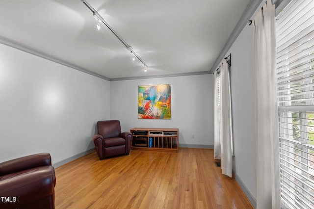 living area with light wood-style floors, rail lighting, crown molding, and baseboards