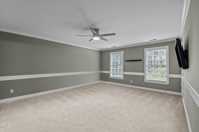 carpeted spare room with a ceiling fan, visible vents, crown molding, and baseboards