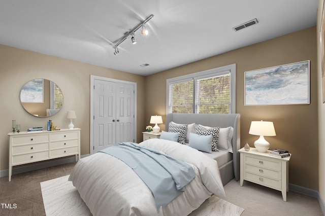 carpeted bedroom with rail lighting, a closet, visible vents, and baseboards