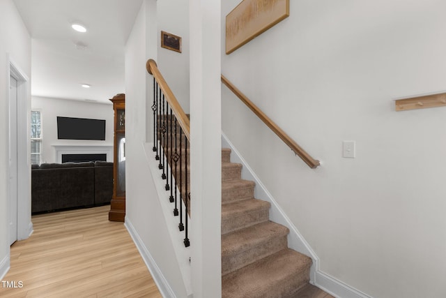 staircase featuring a fireplace, baseboards, wood finished floors, and recessed lighting