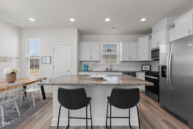 kitchen with stainless steel appliances, a breakfast bar, a sink, a kitchen island, and white cabinetry