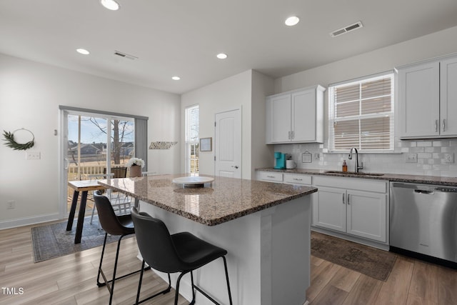 kitchen with visible vents, decorative backsplash, stainless steel dishwasher, a sink, and dark stone countertops