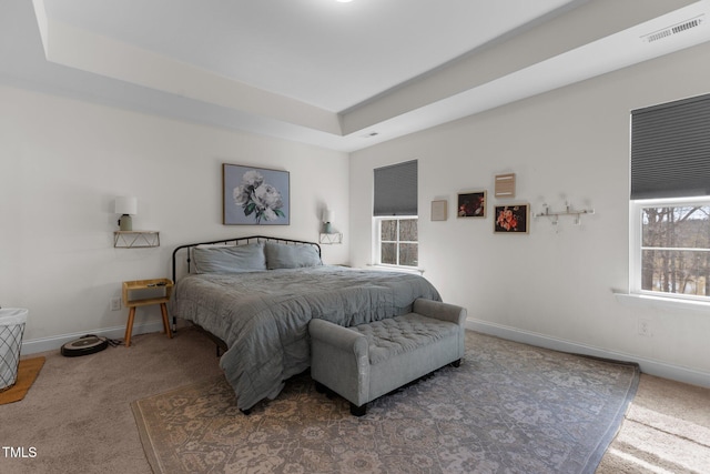 carpeted bedroom with visible vents, a tray ceiling, and baseboards