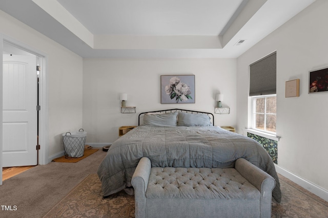 carpeted bedroom with visible vents, a tray ceiling, and baseboards