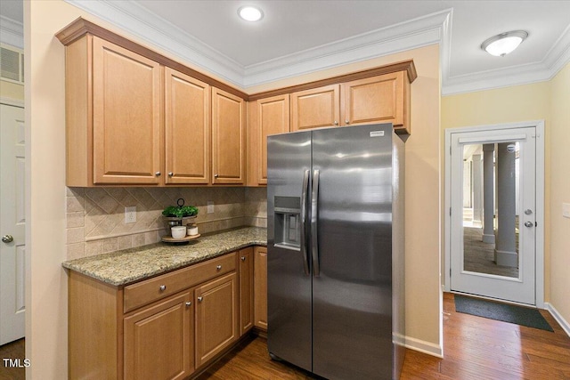 kitchen with light stone countertops, dark wood-type flooring, stainless steel fridge with ice dispenser, ornamental molding, and decorative backsplash