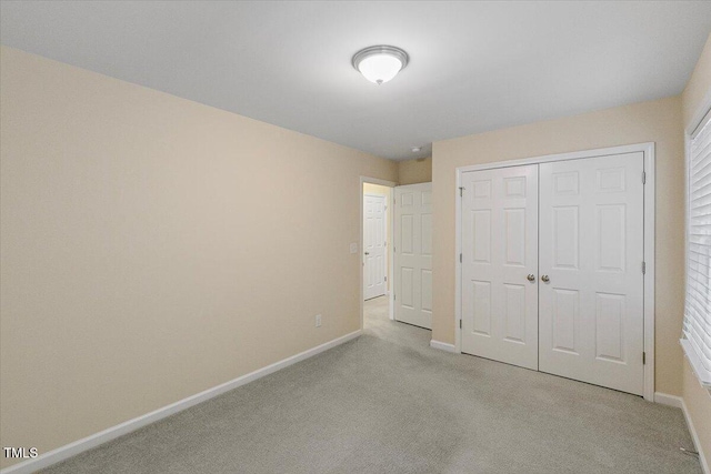 unfurnished bedroom with a closet, light colored carpet, and baseboards