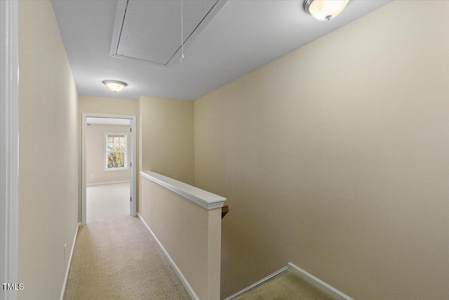 hall with attic access, baseboards, light colored carpet, and an upstairs landing