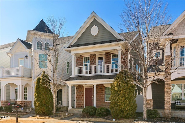 view of front of house featuring a balcony, a standing seam roof, metal roof, and brick siding