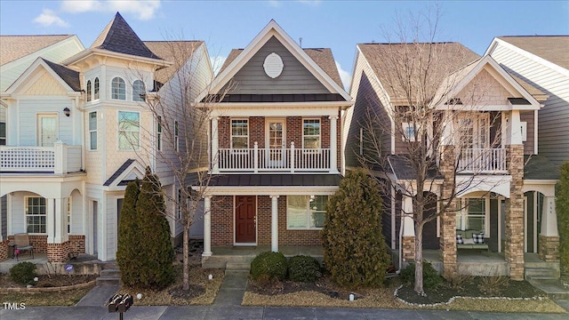 view of front of home featuring metal roof, a porch, a balcony, brick siding, and a standing seam roof