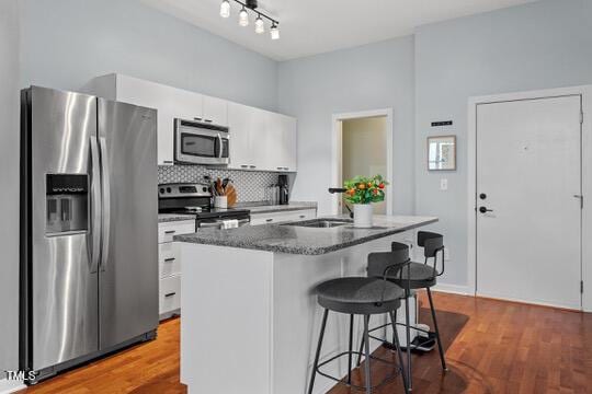 kitchen featuring stainless steel appliances, wood finished floors, white cabinets, a kitchen breakfast bar, and backsplash