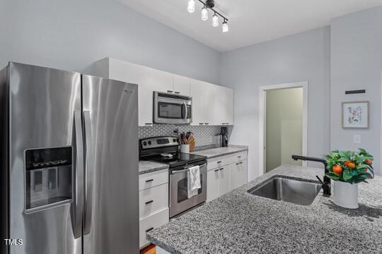 kitchen featuring backsplash, appliances with stainless steel finishes, white cabinets, a sink, and light stone countertops