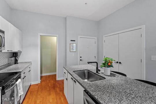 kitchen with light wood-style flooring, light stone counters, white cabinets, and a sink