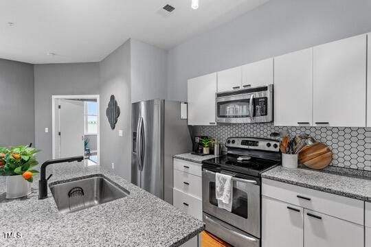 kitchen featuring appliances with stainless steel finishes, white cabinets, a sink, and tasteful backsplash