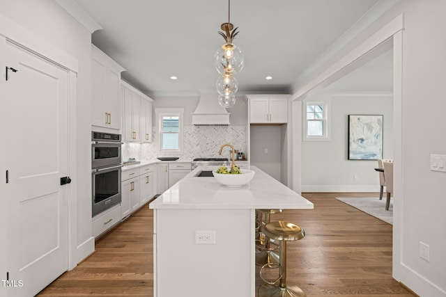 kitchen with a sink, decorative backsplash, crown molding, and custom range hood