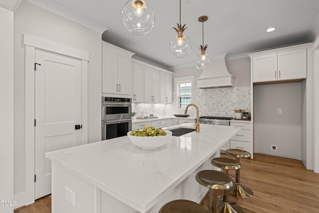 kitchen featuring double oven, white cabinetry, custom range hood, and a sink