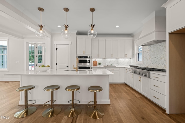 kitchen with premium range hood, light wood finished floors, appliances with stainless steel finishes, crown molding, and light countertops