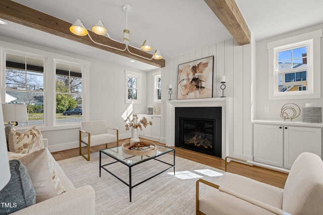 living room featuring beamed ceiling, light wood-type flooring, baseboards, and a glass covered fireplace