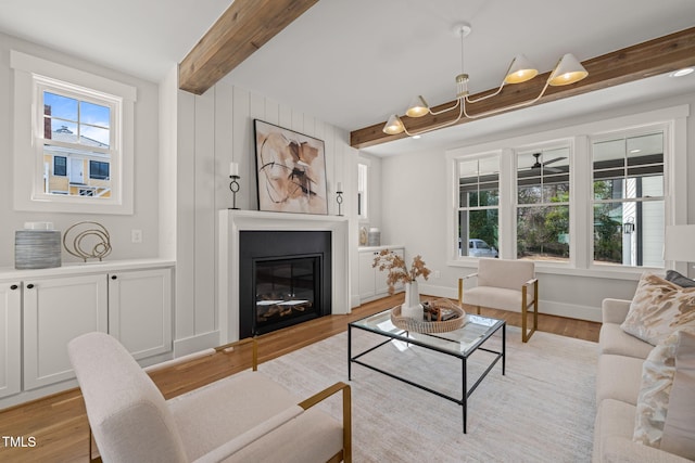 living room featuring beam ceiling, a glass covered fireplace, light wood-style flooring, and a wealth of natural light